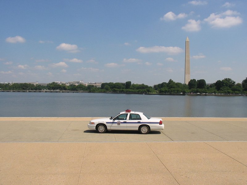 A 2005 archival photograph of a white police patrol cruiser parked along the waterfront in Washington, D.C., with the Washington Monument in the background.